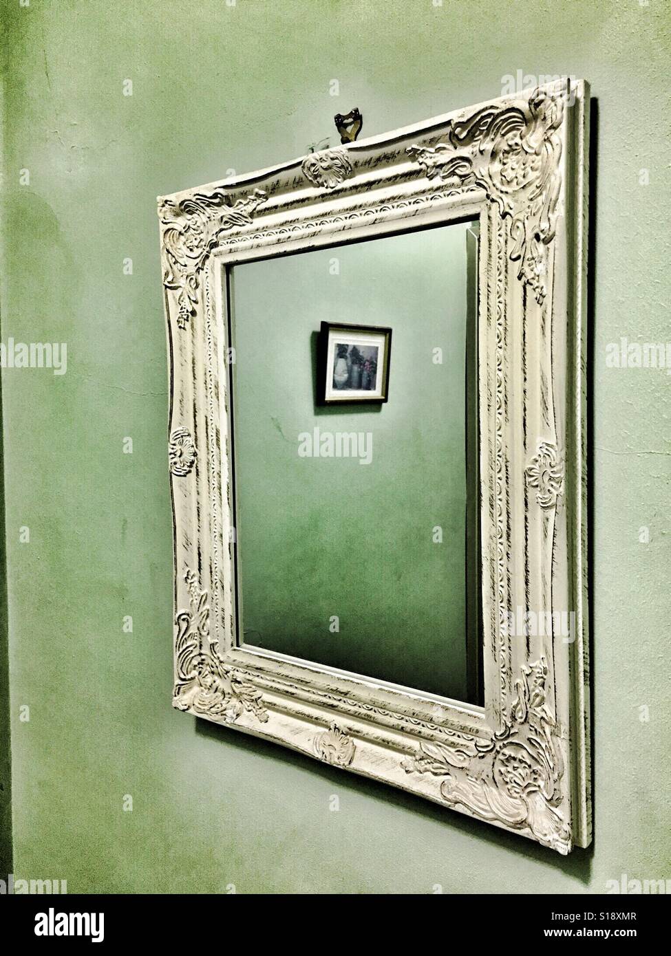 White-framed mirror on a green, painted wall reflecting a small picture - Smartphone Captured Stock Image