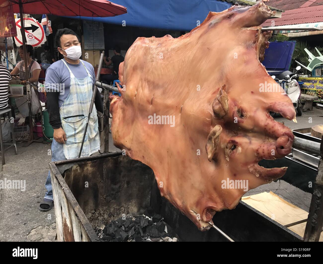 Pig roast area and male chef cooking at a Thai street food market - Smartphone Captured Stock Image