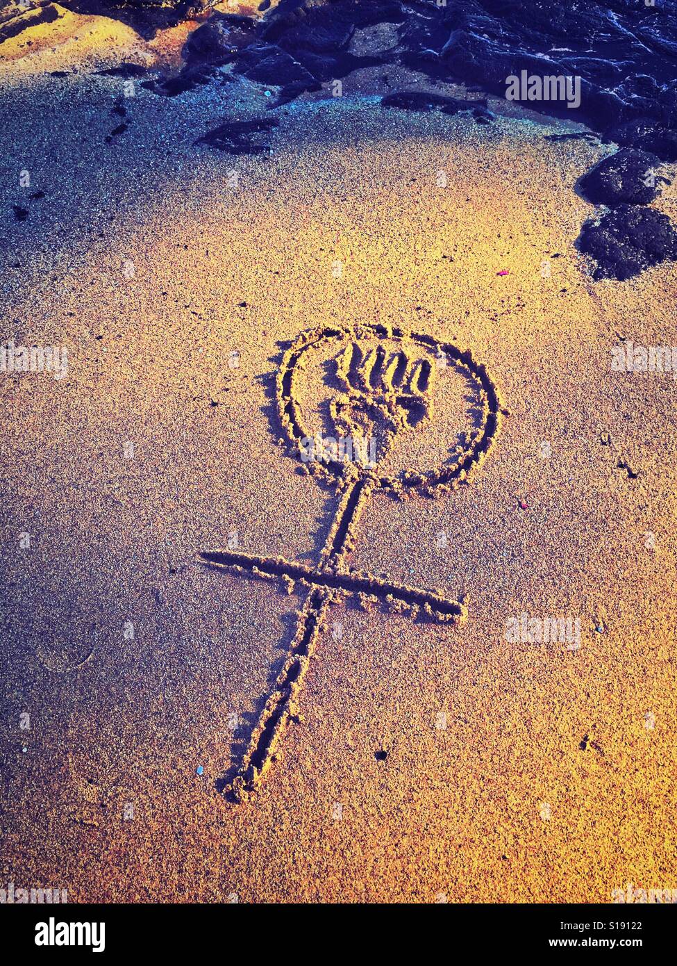 A symbolic stick figure of a woman with power is drawn in the sand. Stock Photo