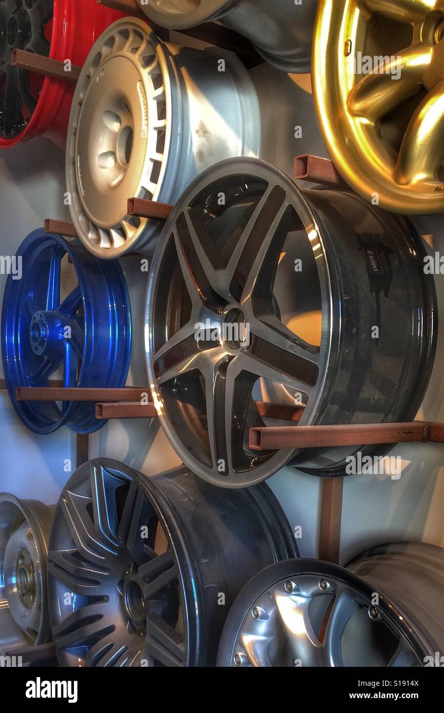 Brightly coloured alloy wheel hubs hanging on a workshop display rack. - Smartphone Captured Stock Image