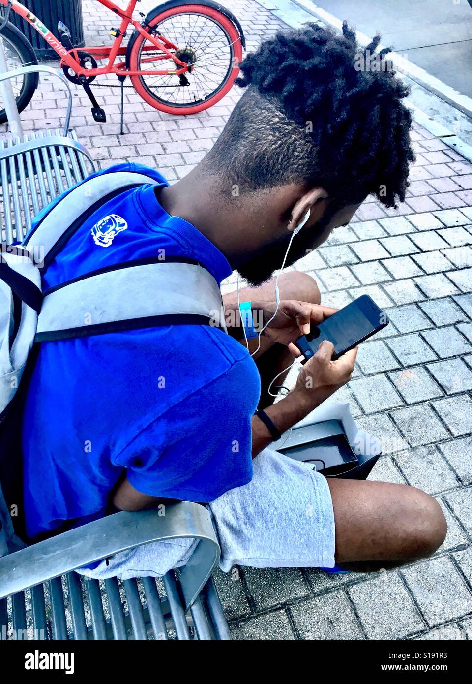 Urban kid on his smart phone waiting for the bus - Smartphone Captured Stock Image
