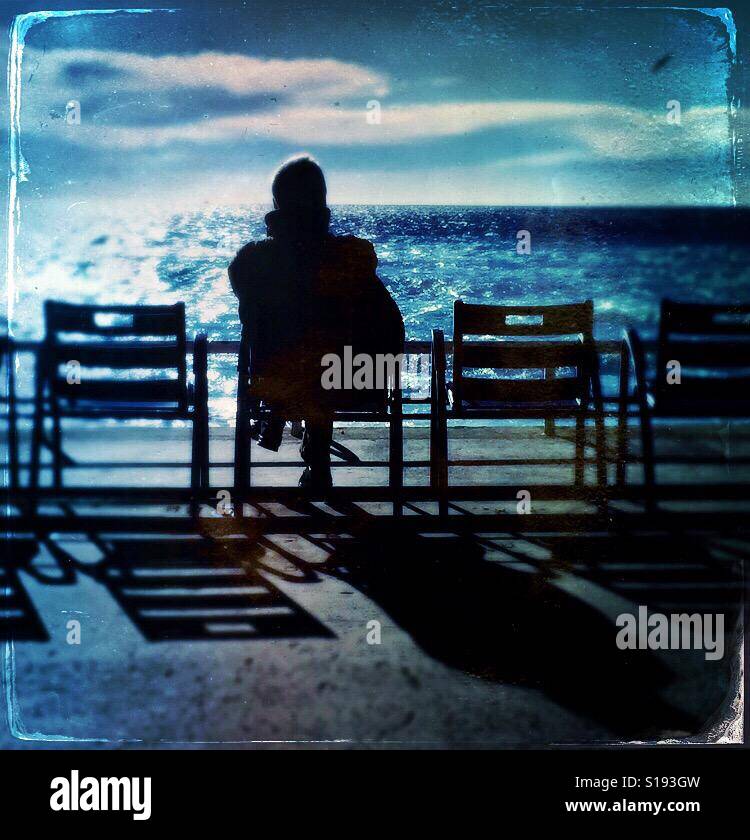 Man on a chair looking out to the Mediterranean Sea with blue skies and high clouds - Smartphone Captured Stock Image