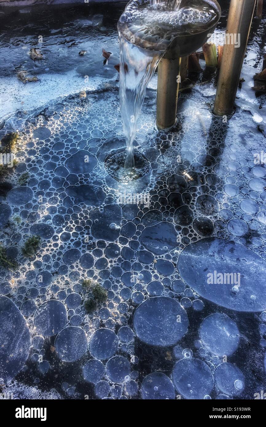 Bubbles formed by a fountain under thick ice on a garden pond in winter Stock Photo