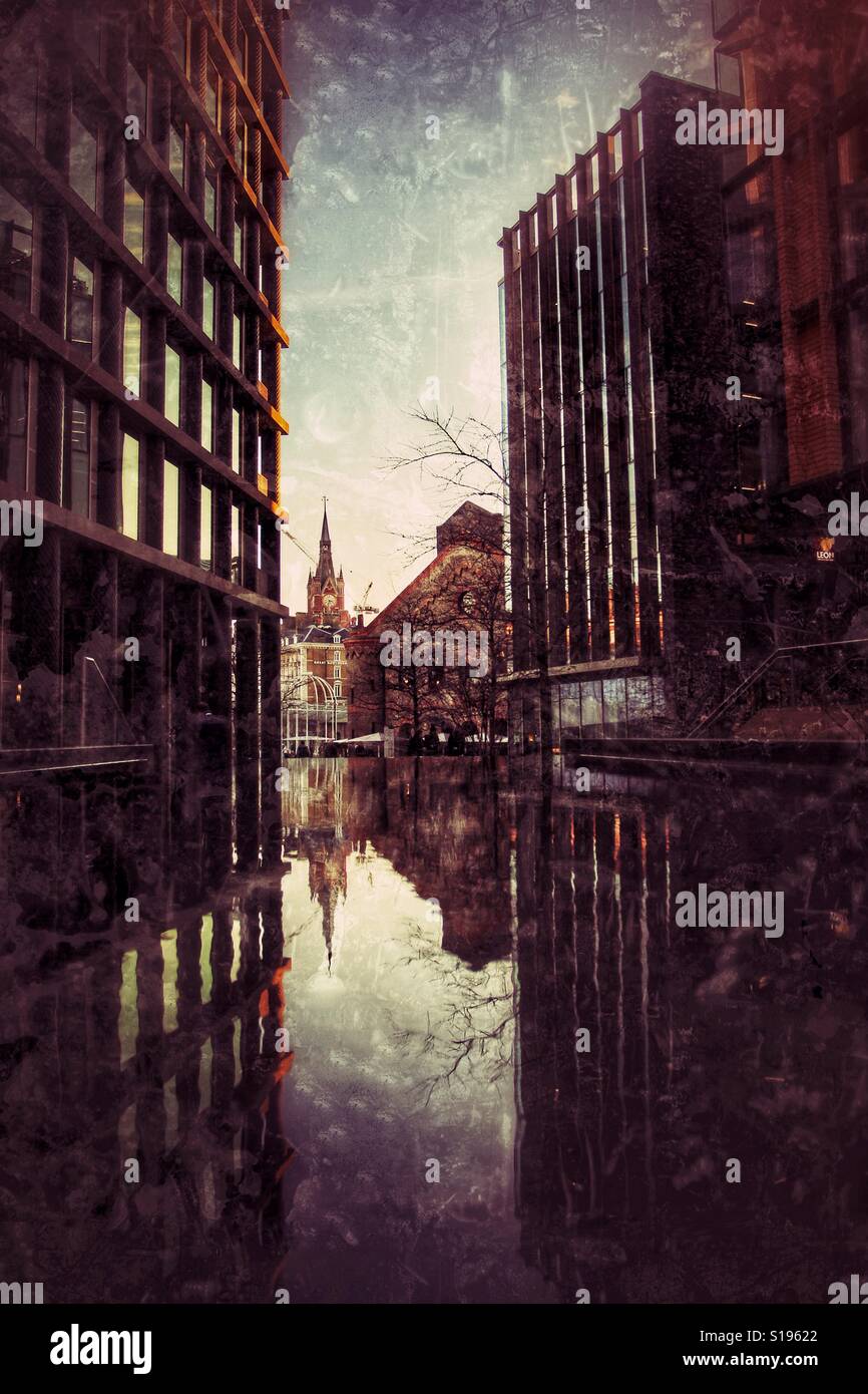 An eerie, urban view of St Pancras in London with modern skyscrapers reflected in a pool of water with a grunge texture - Smartphone Captured Stock Image