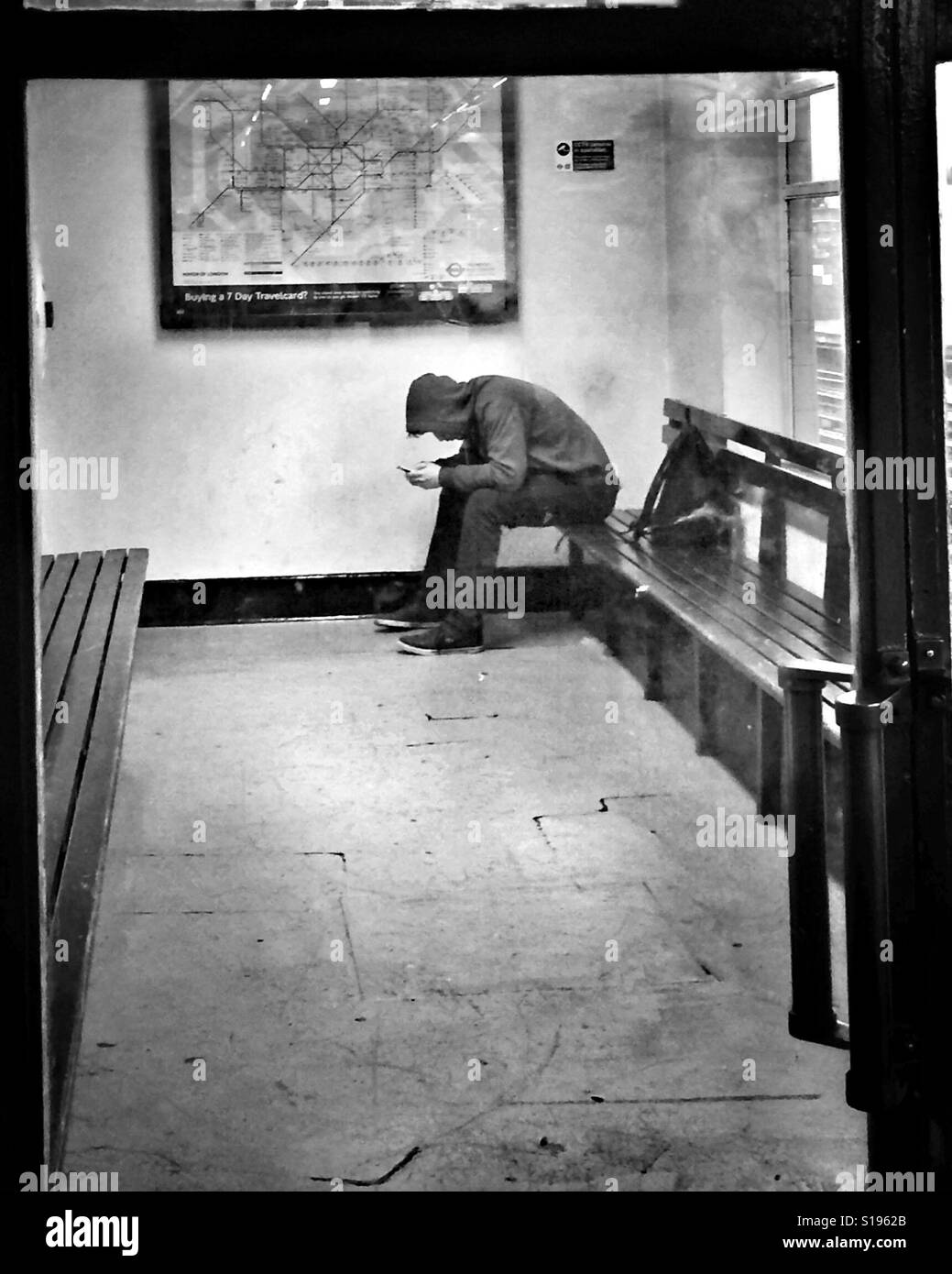 Youth in hooded top on mobile in waiting room - Smartphone Captured Stock Image