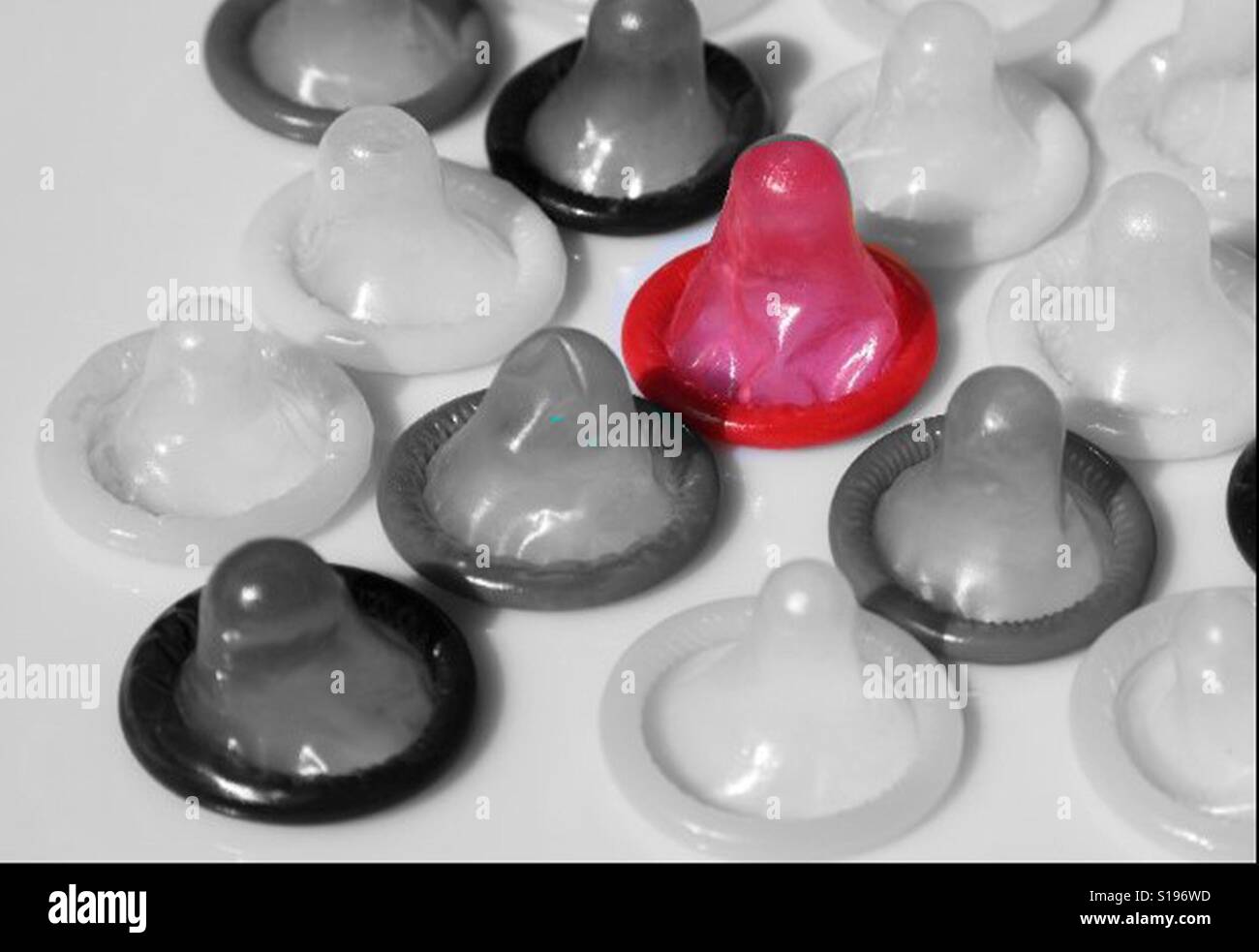 One red condom in a selection of black and white condoms Stock Photo