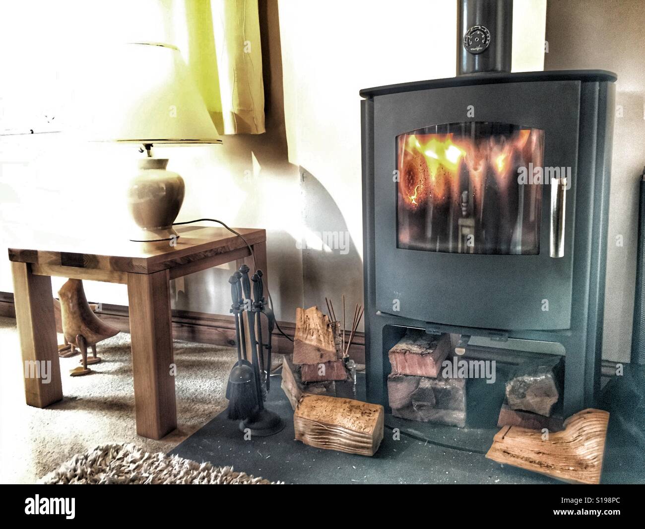 House interior. Sun streaming in to a room with a multi fuel burner, lit - Smartphone Captured Stock Image