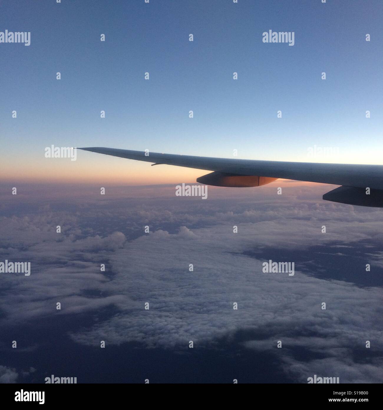 Airplane wing flying above clouds at first light, sunrise Stock Photo