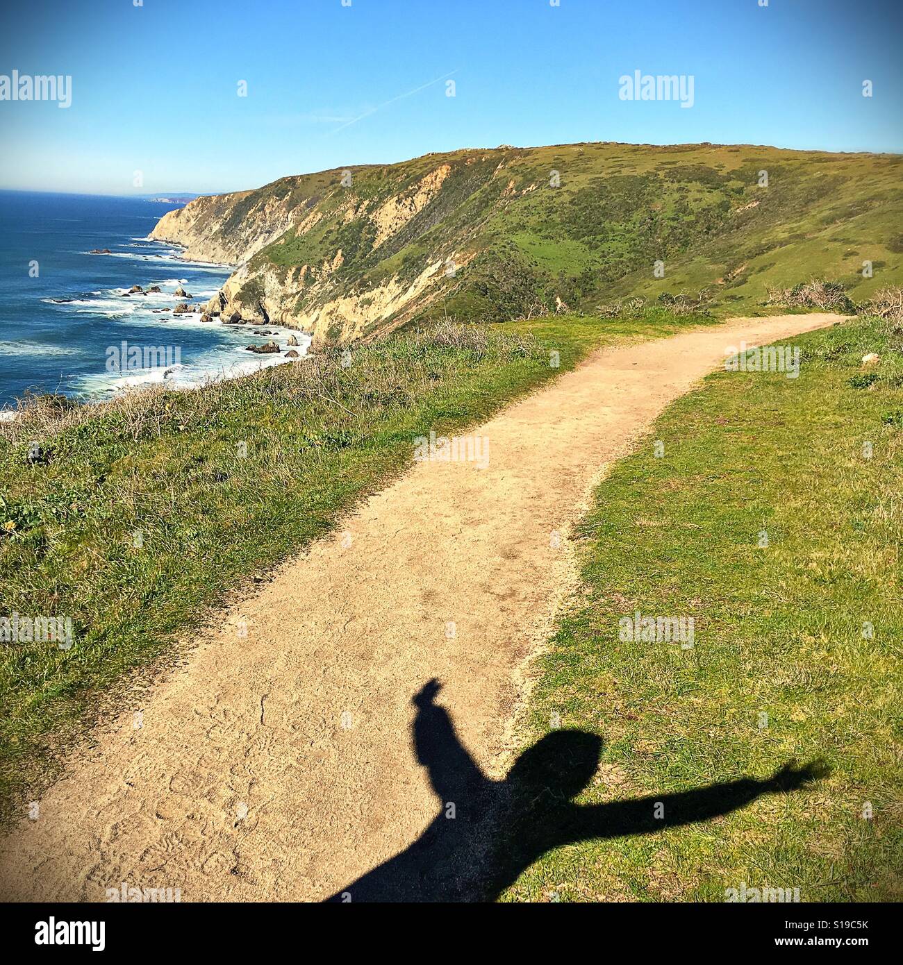 The shadow of a person with arms open wide on the rugged coast of northern California. Stock Photo