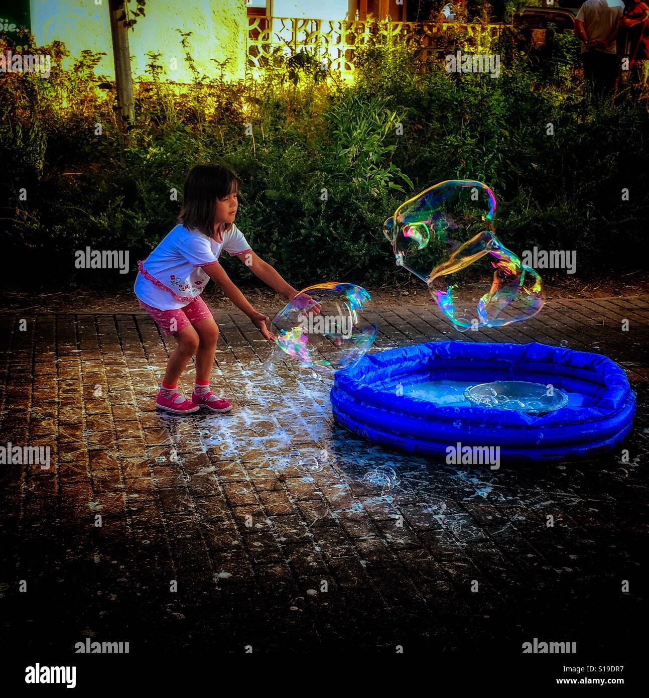 Young girl playing with a soap bubble in a small pool at the street