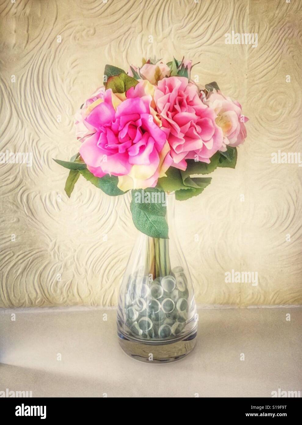Pink Artificial Roses In A Crystal Vase Set Against A Textured