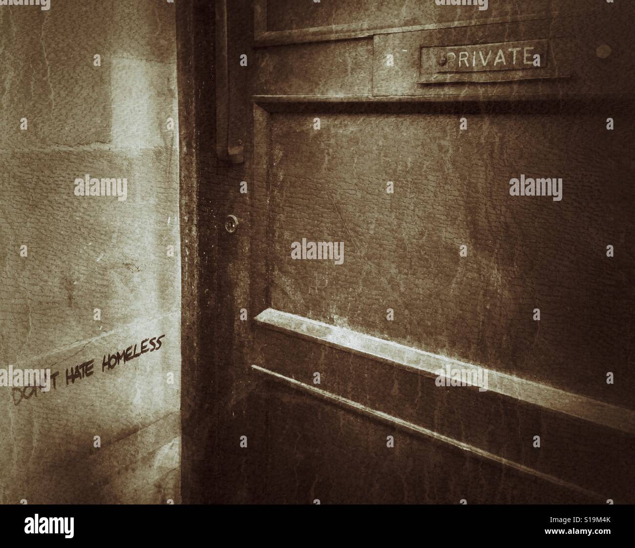 A grungey sepia photograph of graffiti reading 'DON'T HATE HOMELESS' on a wall next to a door marked 'PRIVATE' in a town in the UK Stock Photo