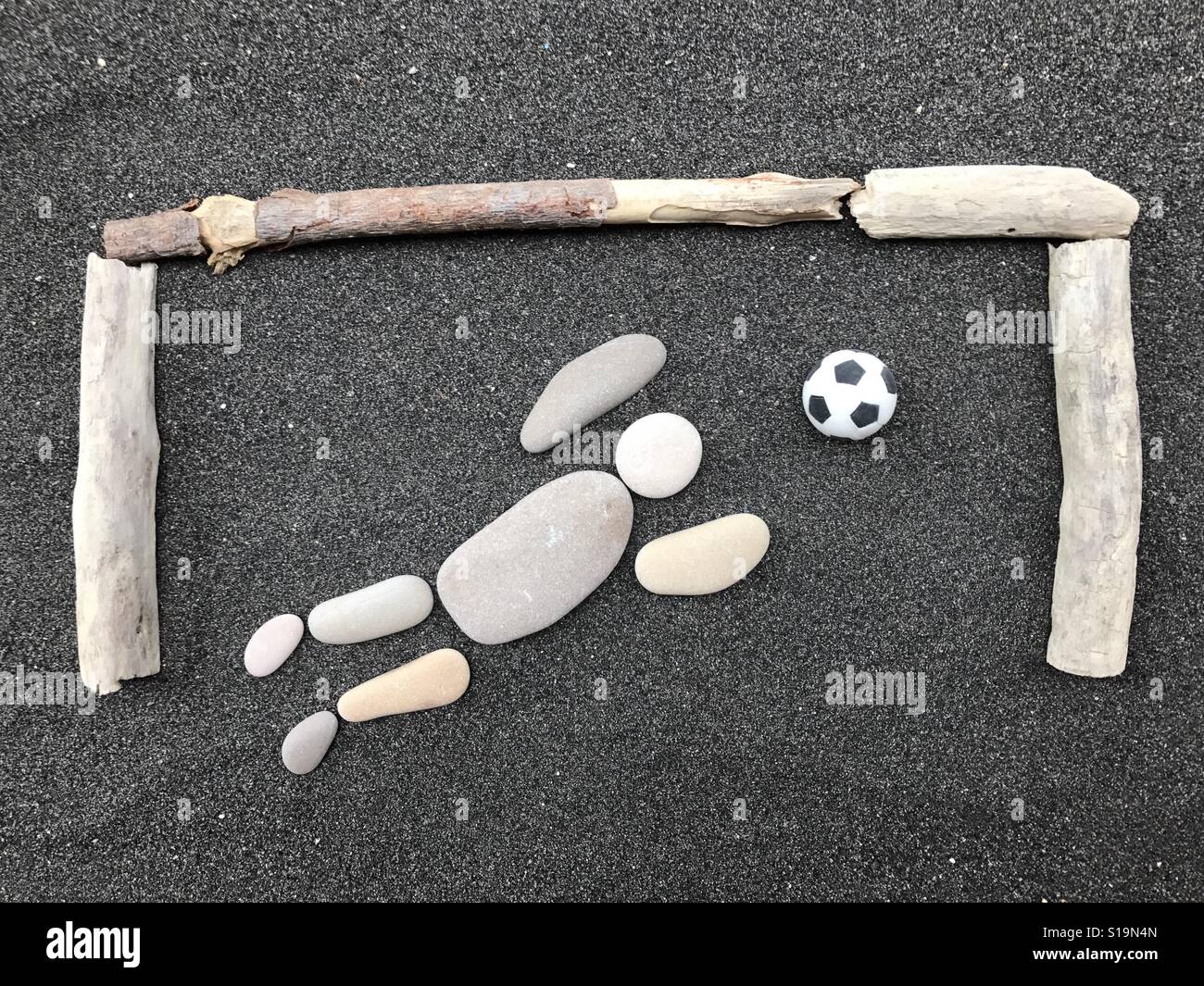 The goalkeeper, creative composition of stones and pebbles over black volcanic sand - Smartphone Captured Stock Image