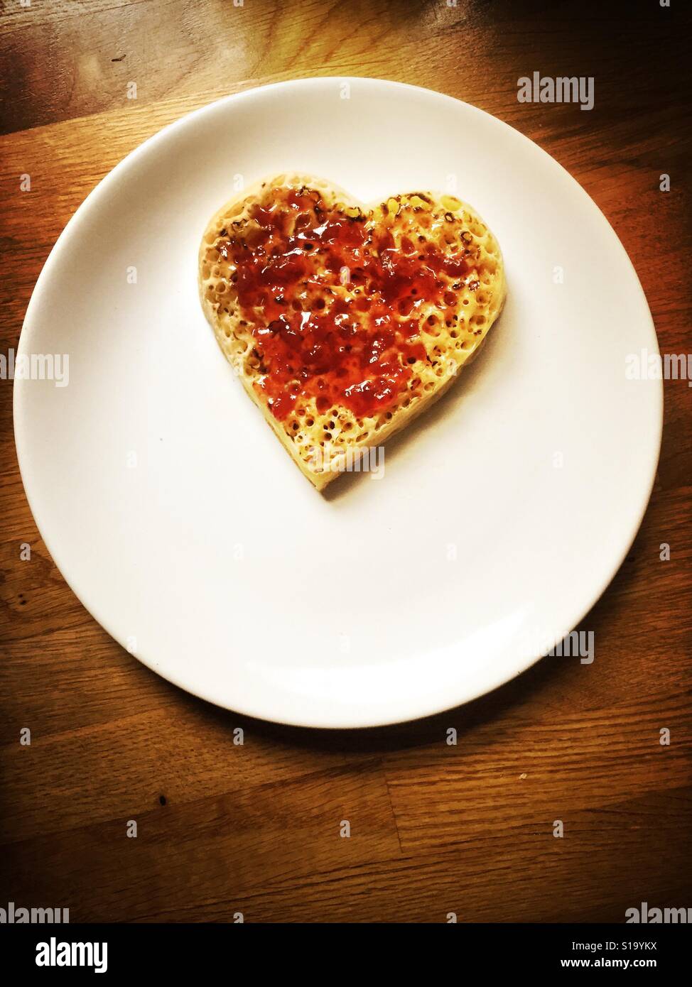 A crumpet in the shape of a heart covered with strawberry jam. Stock Photo