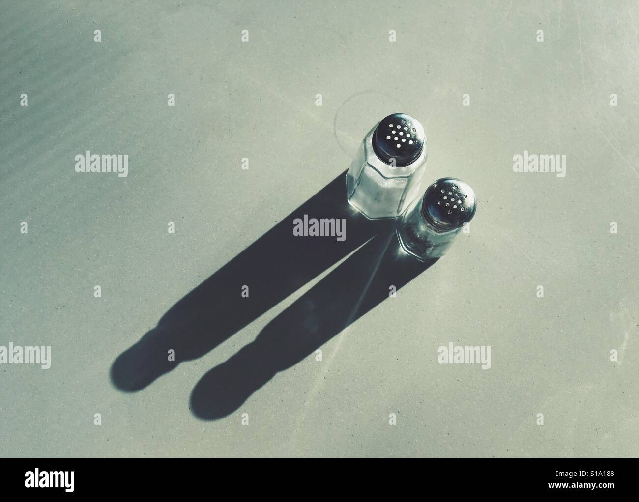 High angle view of salt and pepper shakers casting long shadows on a table Stock Photo