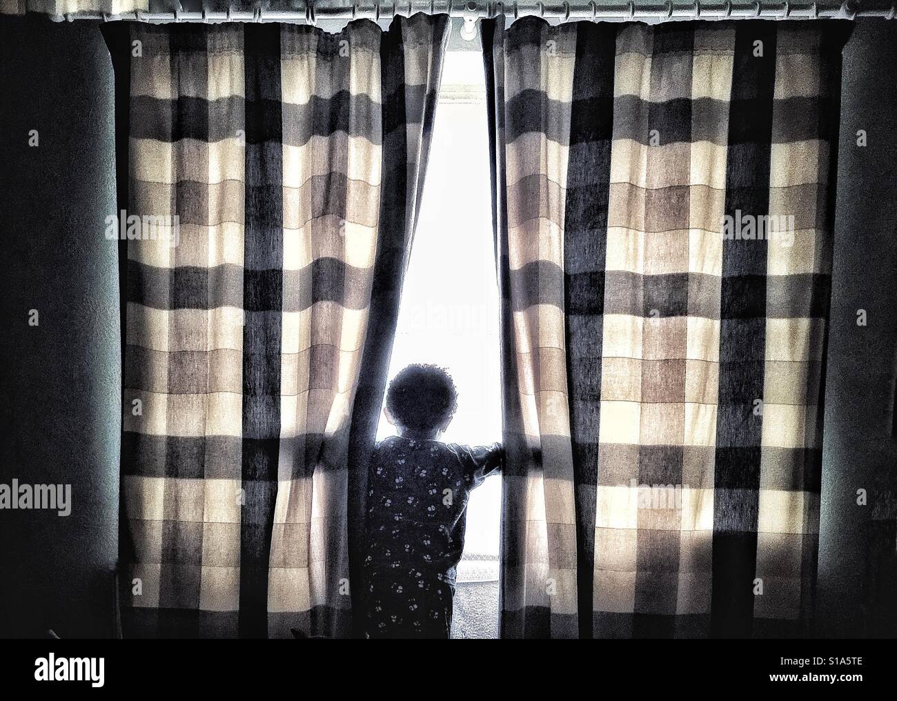 A little boy in pyjamas at a window. Stock Photo