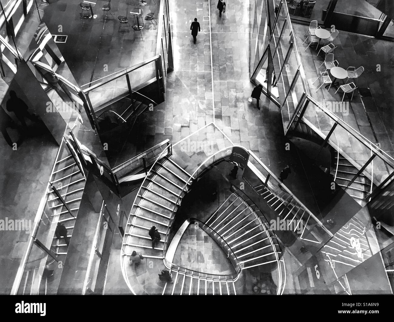 Black and white photo of people walking on the spiral staircase at One New Change shopping mall in the City of London, England, UK. Stock Photo