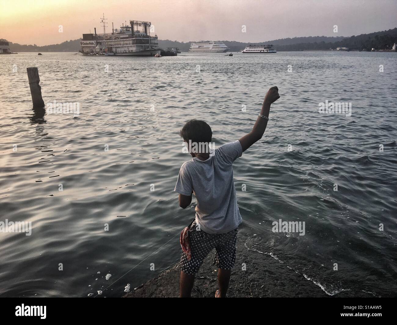 A fisherman tries to catch a fish in front of one of the boats used as a casino - Smartphone Captured Stock Image