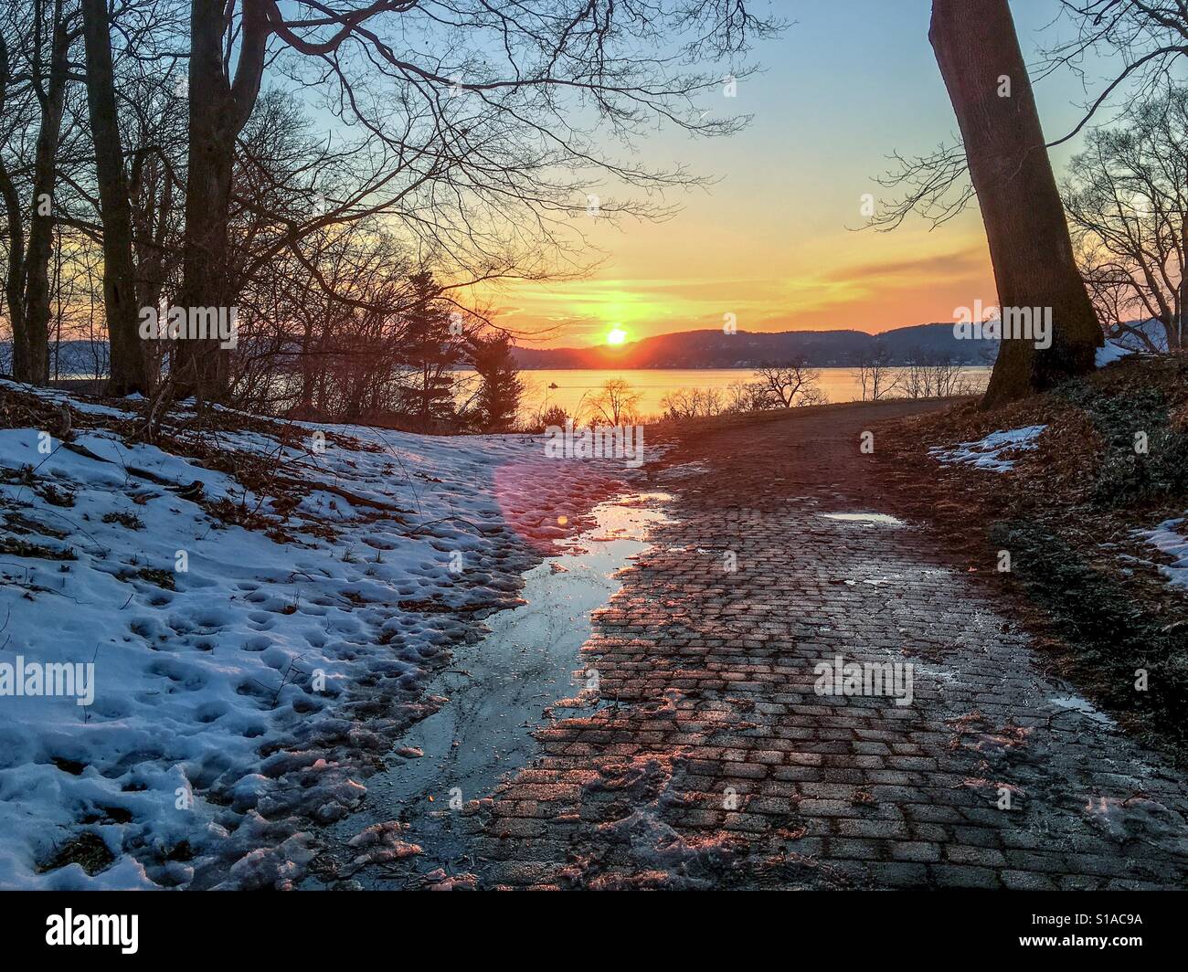 Beautiful sunset in the Hudson River Valley reflections in melting snow puddles yellow orange pink sky - Smartphone Captured Stock Image