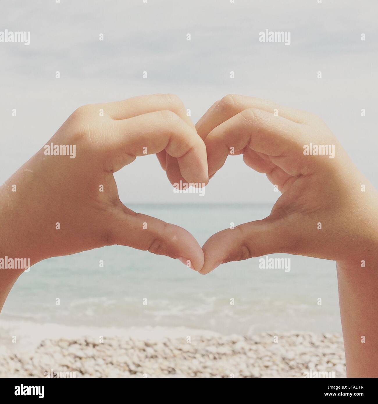 Heart shape with girl hands by the beach Stock Photo