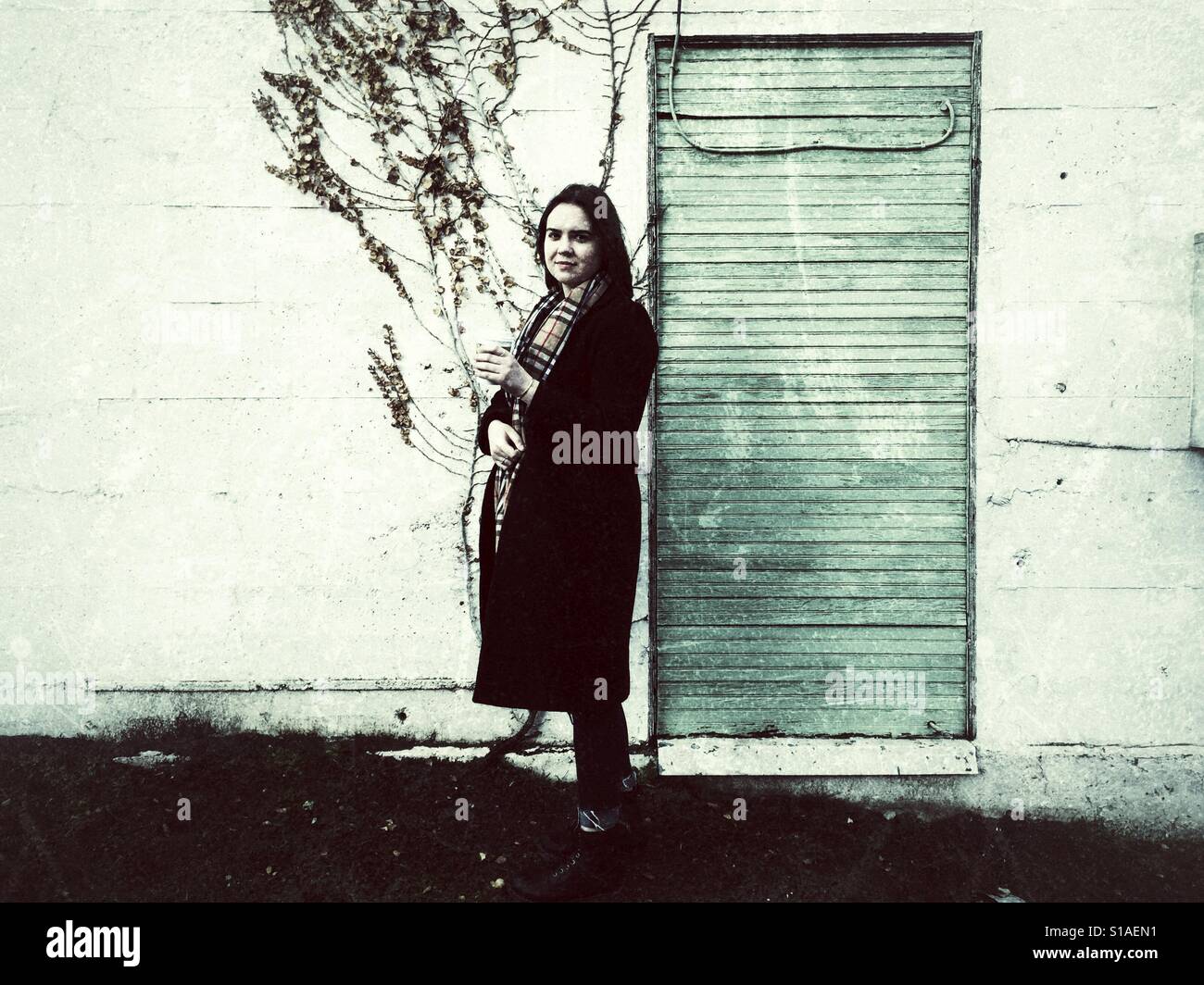 Young woman holding cup of coffee wearing long coat and scarf - Smartphone Captured Stock Image