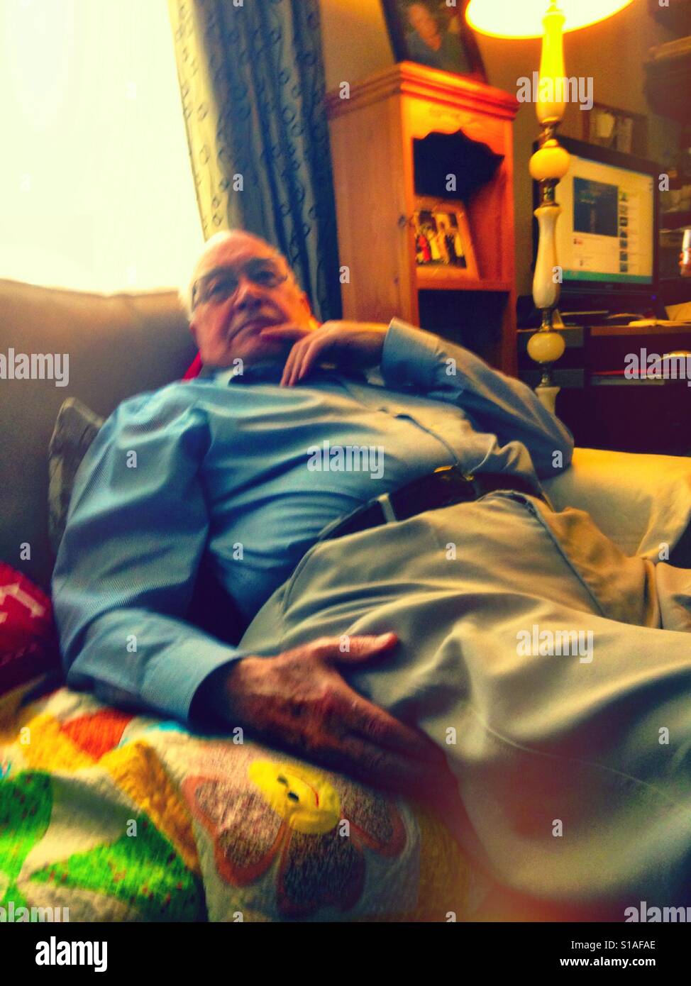 An older gentleman relaxing on a sofa watching TV. - Smartphone Captured Stock Image