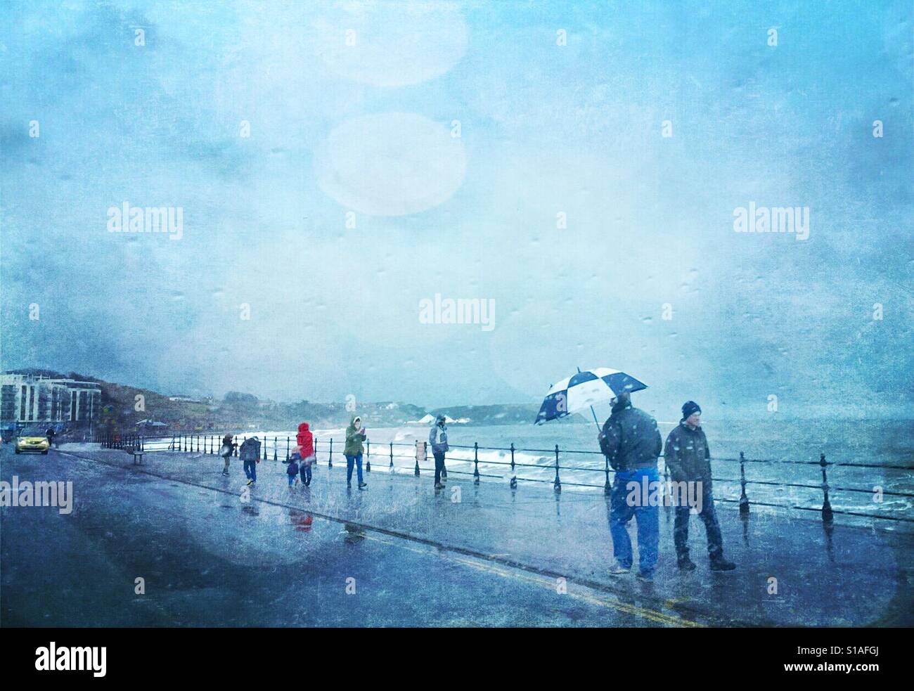 People walking along the seafront in rain and wind with a high sea. Stock Photo