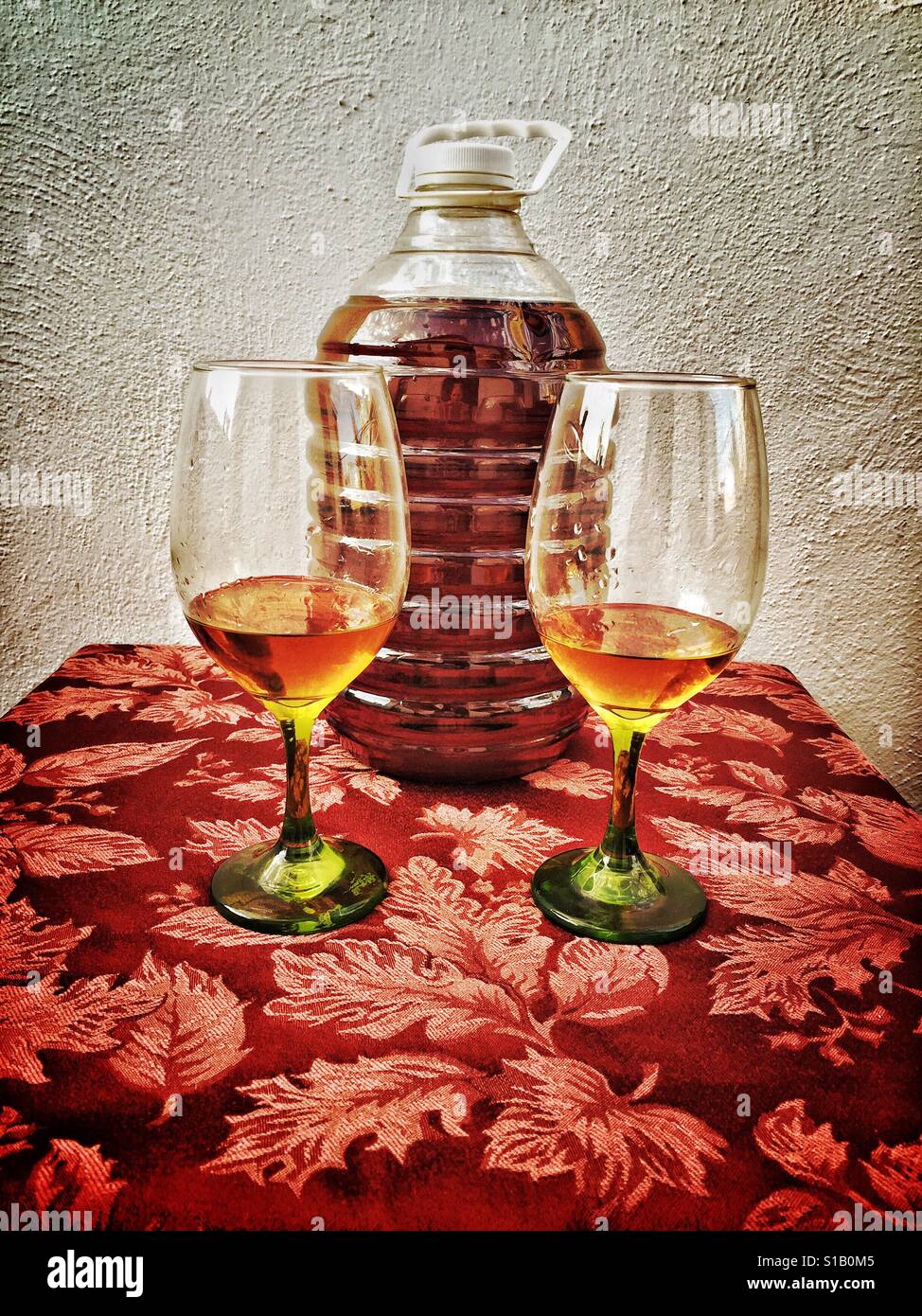 Two glasses of extra añejo sipping tequila are placed in front of a five litre container of tequila. Stock Photo