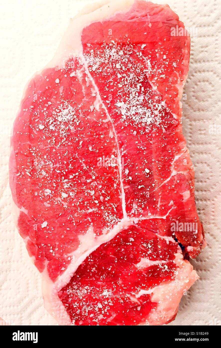 Raw ribeye beef steak on prep board covered in kosher salt Stock Photo