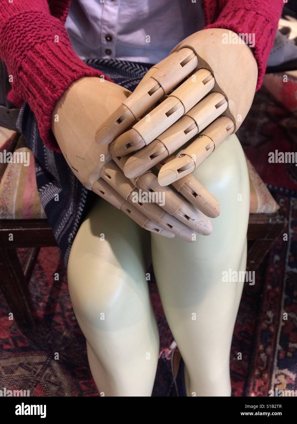A pair of wooden, dummy hands resting on a female mannequins knees. - Smartphone Captured Stock Image