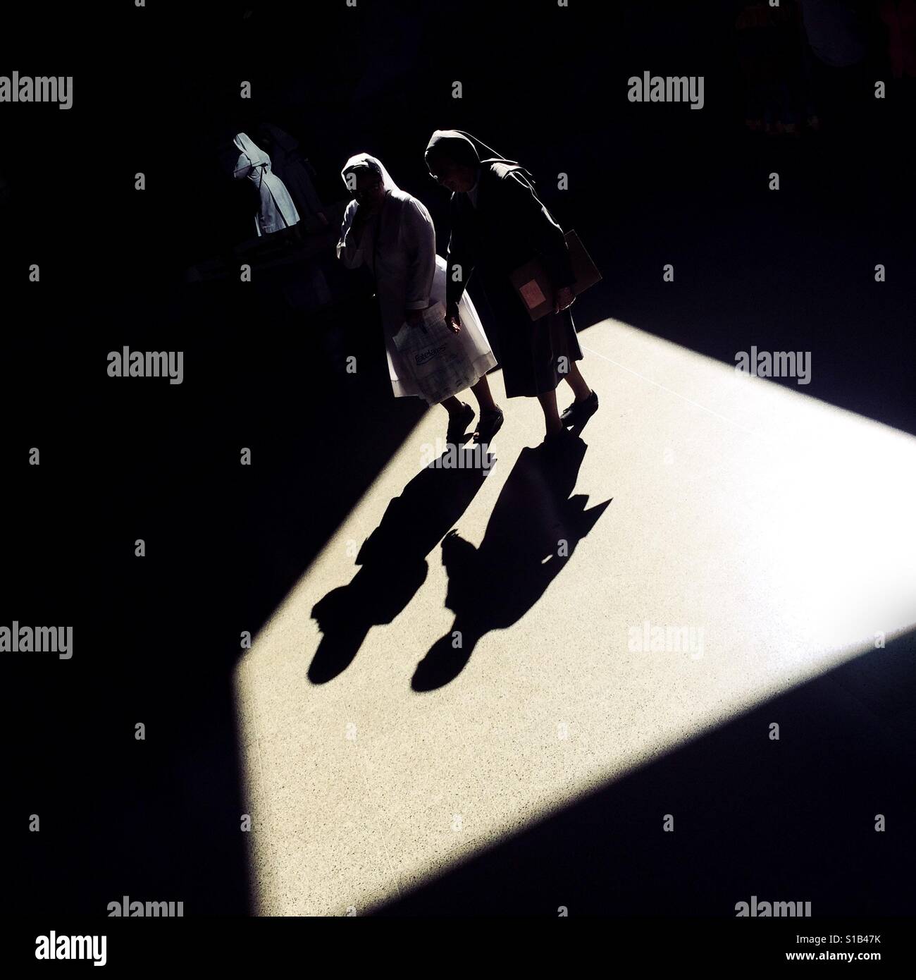 Colombian nuns walk through a beam of light thrown on the platform of San Antonio metro station in Medellín, Colombia, 13 December 2016. Stock Photo
