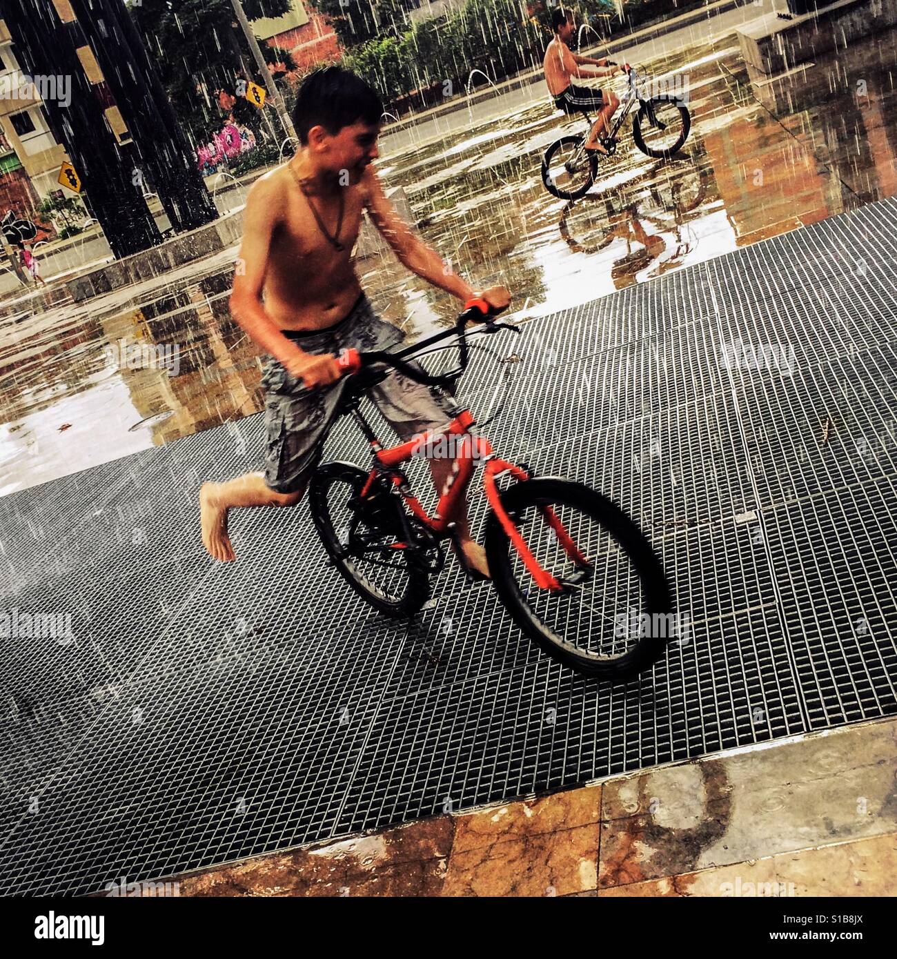 Colombian boys perform tricks on BMX bikes during the rain in Parque Chimeneas, Itagüí, Colombia, 19 November 2016. Stock Photo