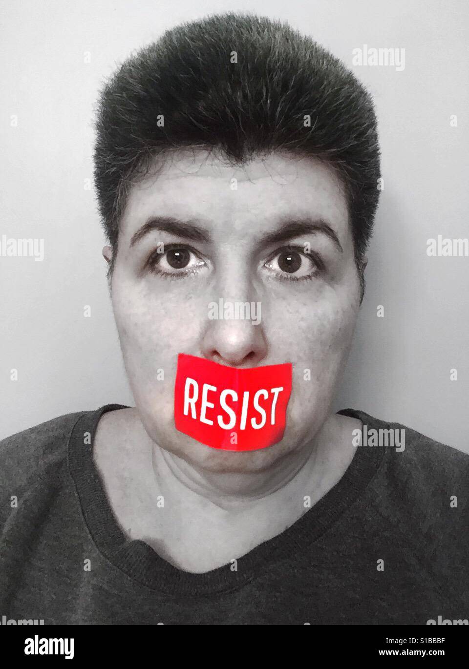 A black and white portrait of a middle aged woman with a red 'Resist' sticker covering her mouth Stock Photo
