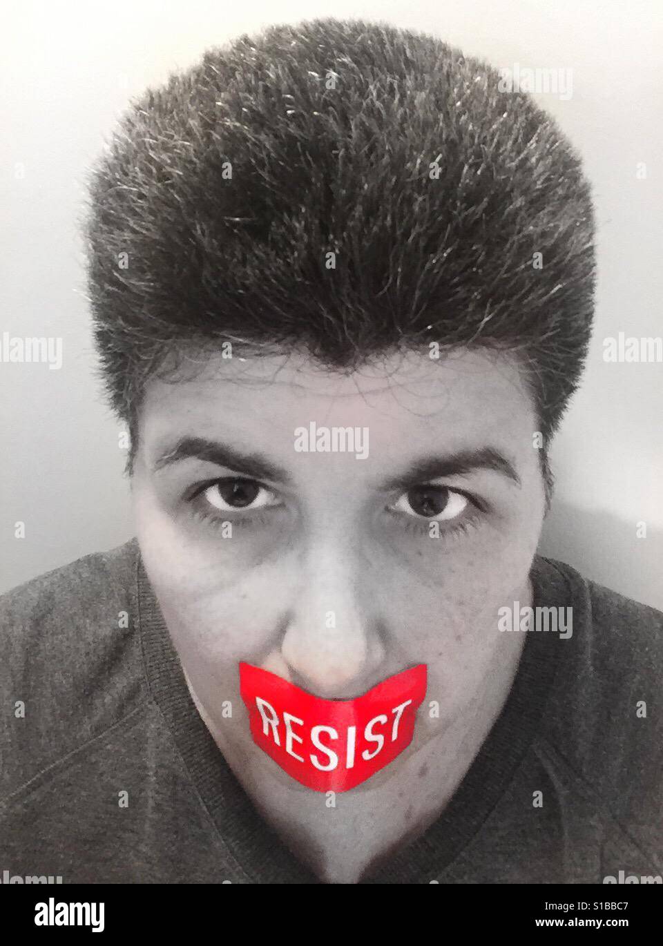 A black and white portrait of a middle aged woman with a red sticker over her mouth that says 'resist' - Smartphone Captured Stock Image