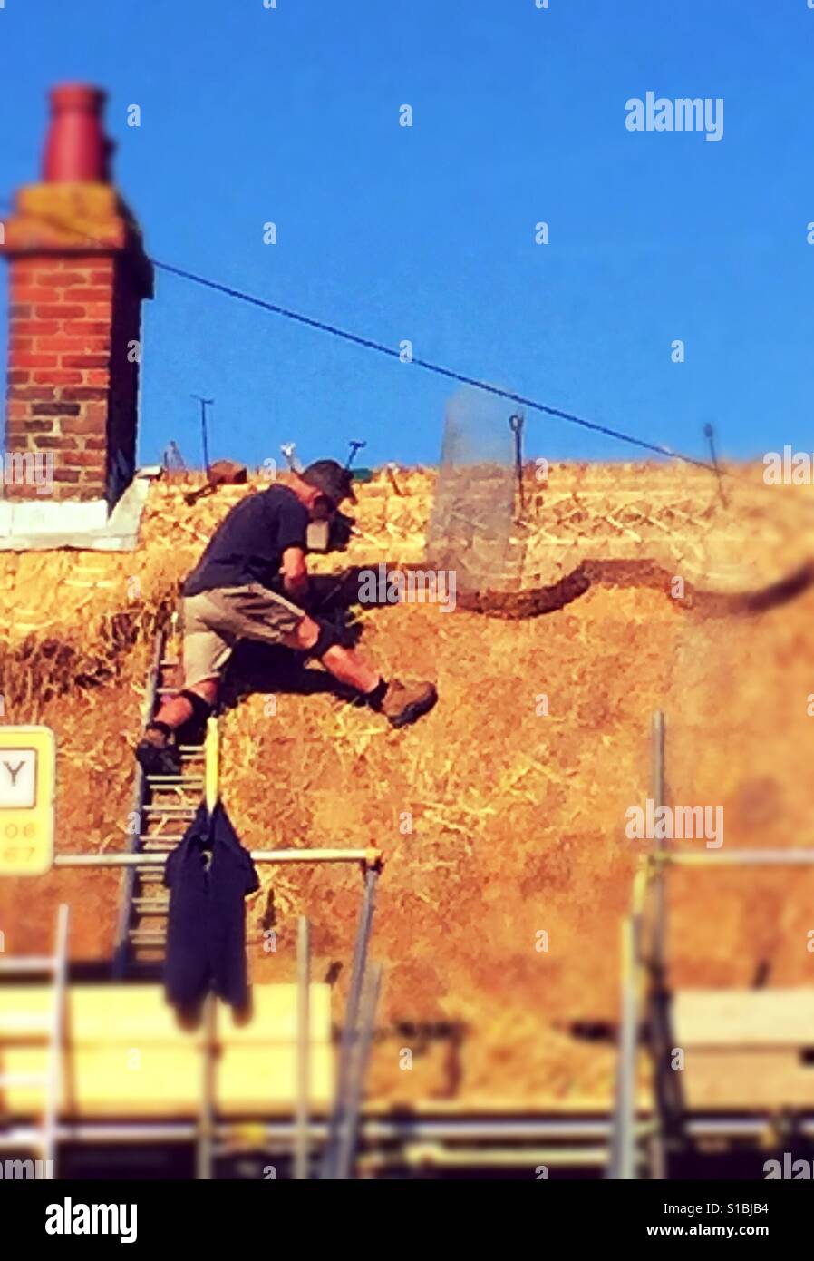 Man thatching roof in spring sunshine - Smartphone Captured Stock Image