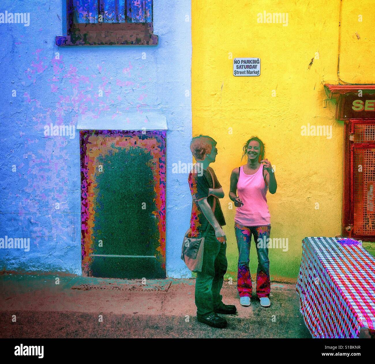 Artistic rendering of scene in street Market in Brighton, Sussex , UK with two young people stopping for a chat and a cigarette in front of a second hand shop and table on the sidewalk. - Smartphone Captured Stock Image