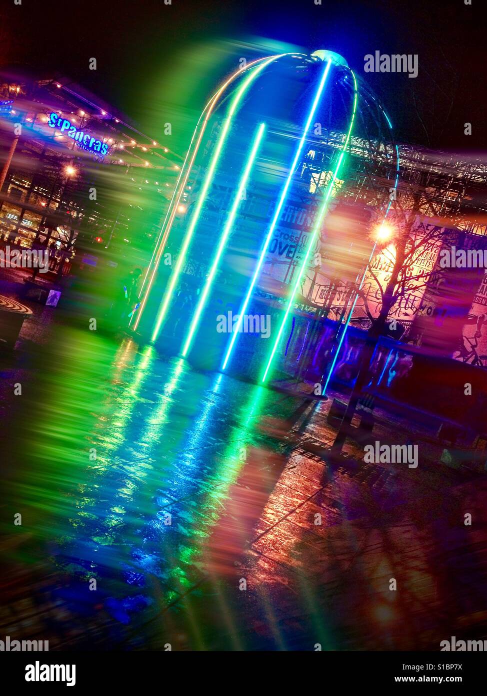 A large birdcage structure illuminated with neon lights on a wet