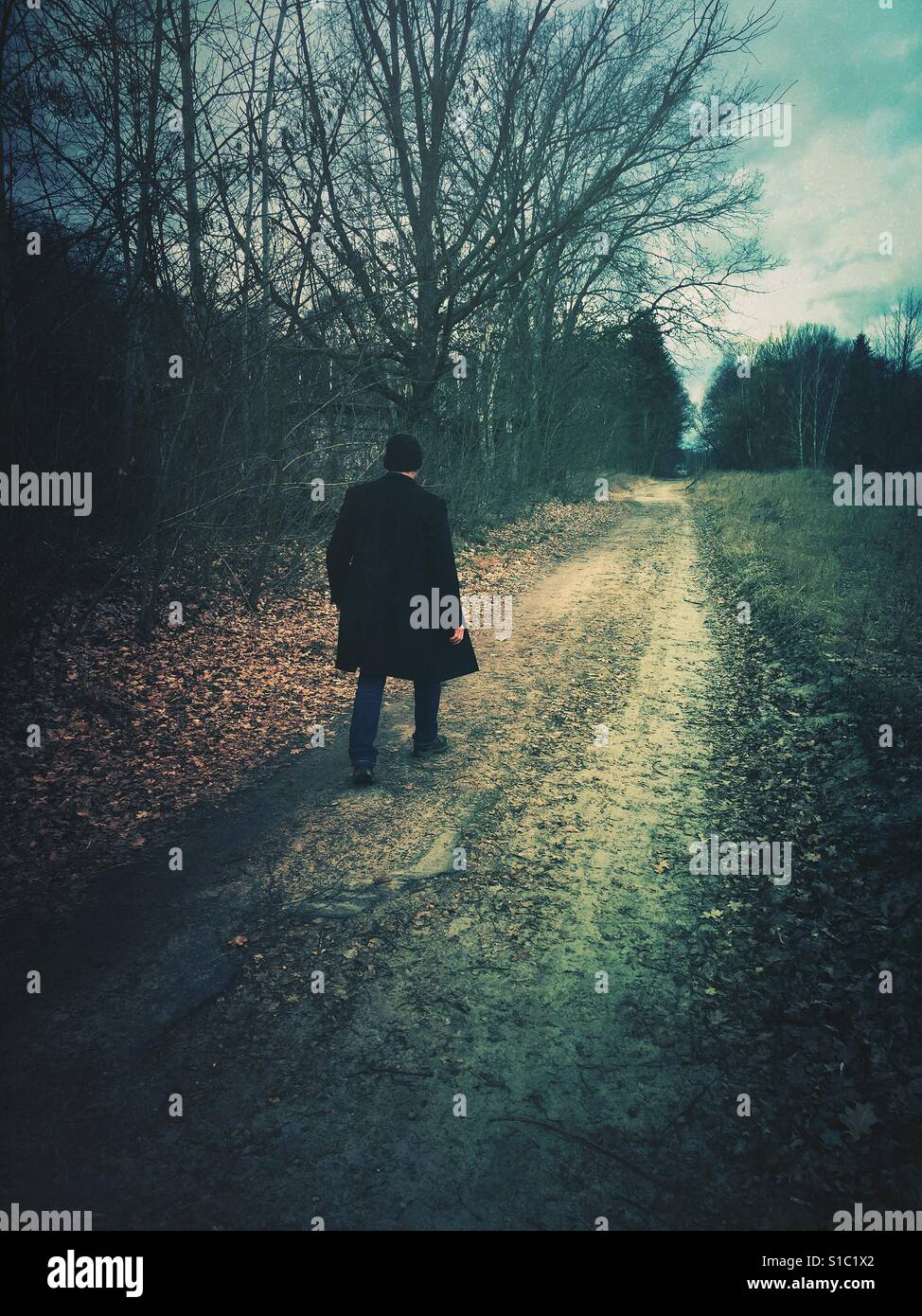 Rear view of a man wearing a coat walking away on a countryside road - Smartphone Captured Stock Image