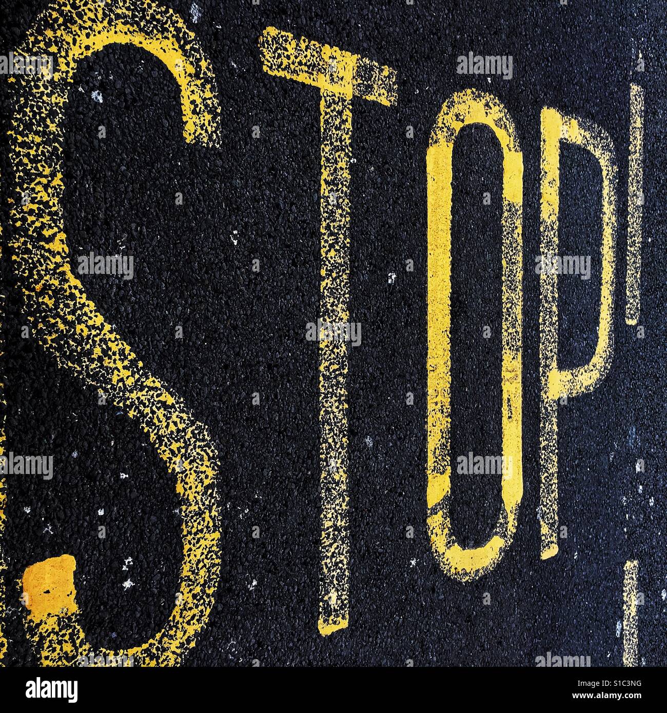 Yellow painted road marking sign on black Tarmac depicting the word Stop. Stock Photo