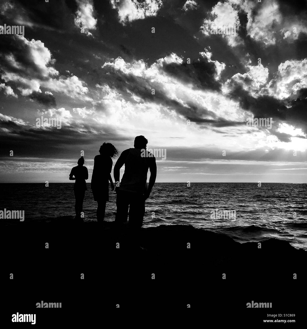 Sunset with 3 people looking out at ocean Stock Photo - Alamy