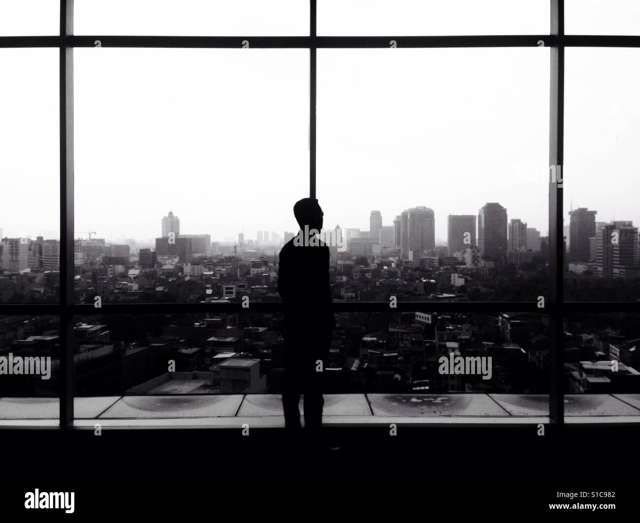Silhouette of Man Looking Out The Window to See Cityscape Landscape - Black and White Stock Photo
