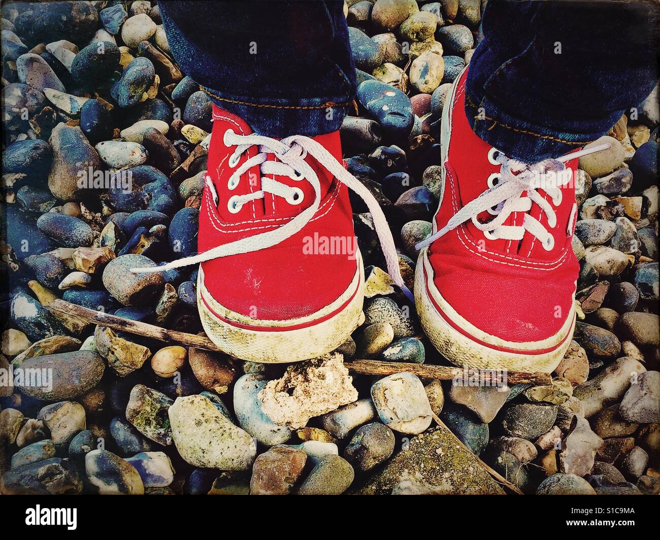 Toddlers red trainers on stones with one lace undone Stock Photo
