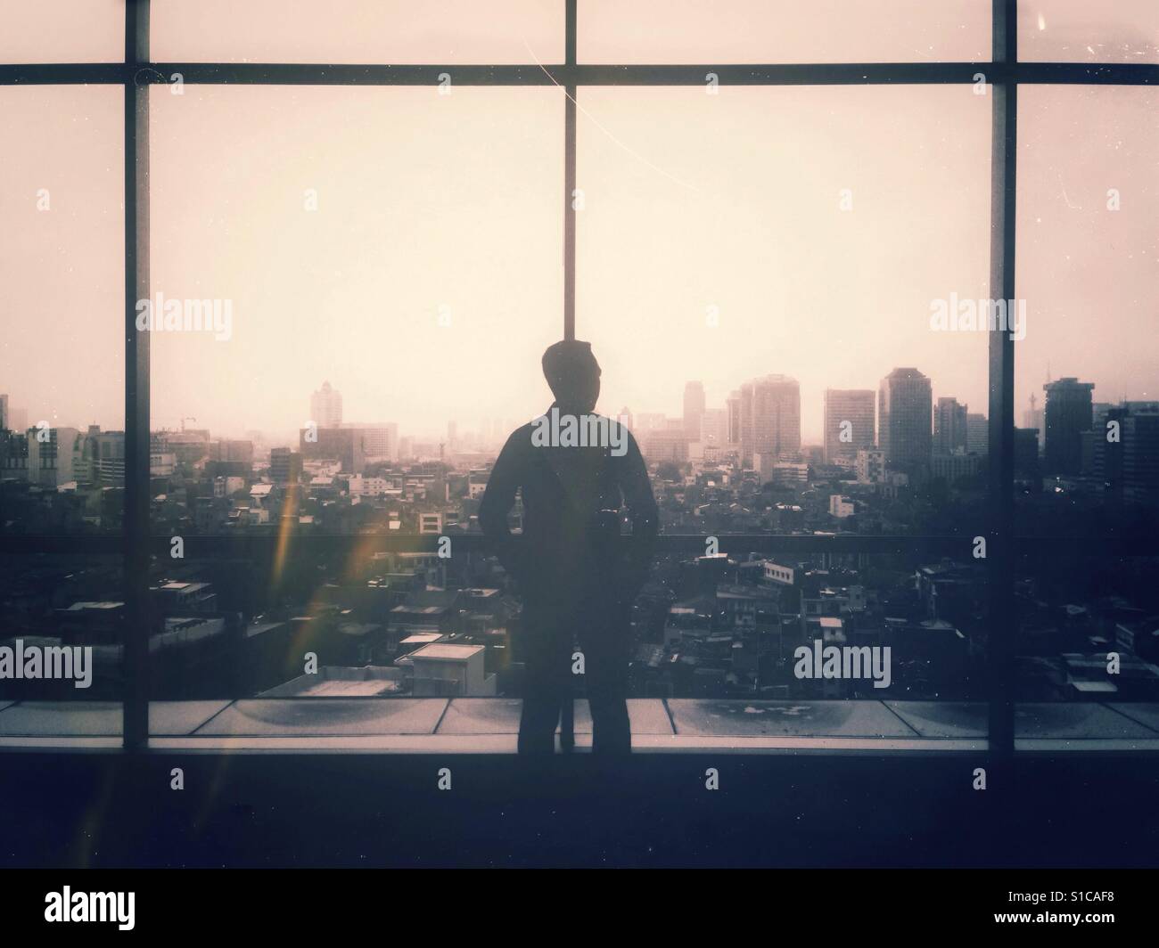 Silhouette of Man Standing and Looking Out the Big Window with Cityscape Landscape in Background Stock Photo
