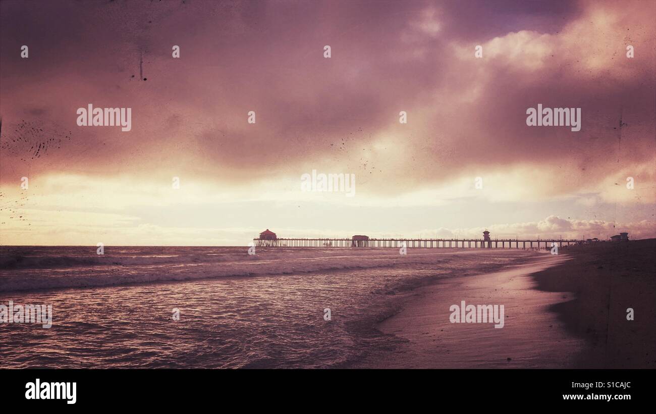 Sandy beach by the ocean with wooden pier in the distance. Vintage edit. 16x9 crop. Stock Photo