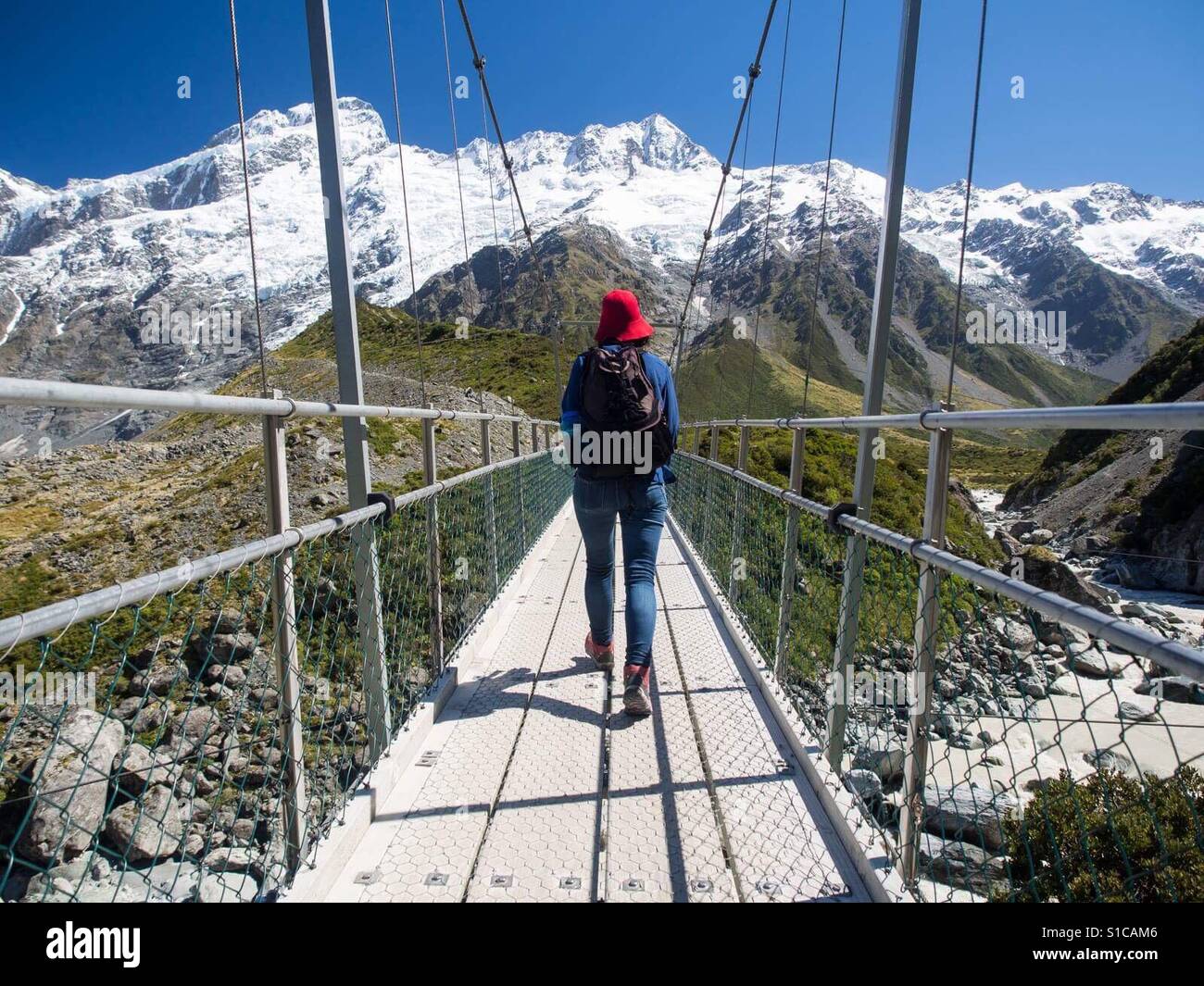 Female hiker walking on Suspension bridge at Mount Cook National Park in South Island New Zealand on a sunny day hiking New Zealand - Smartphone Captured Stock Image