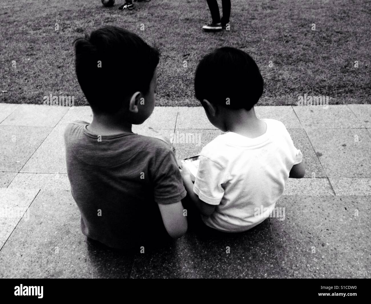 Two Kids Playing Gadget on the Park - Black and White Stock Photo