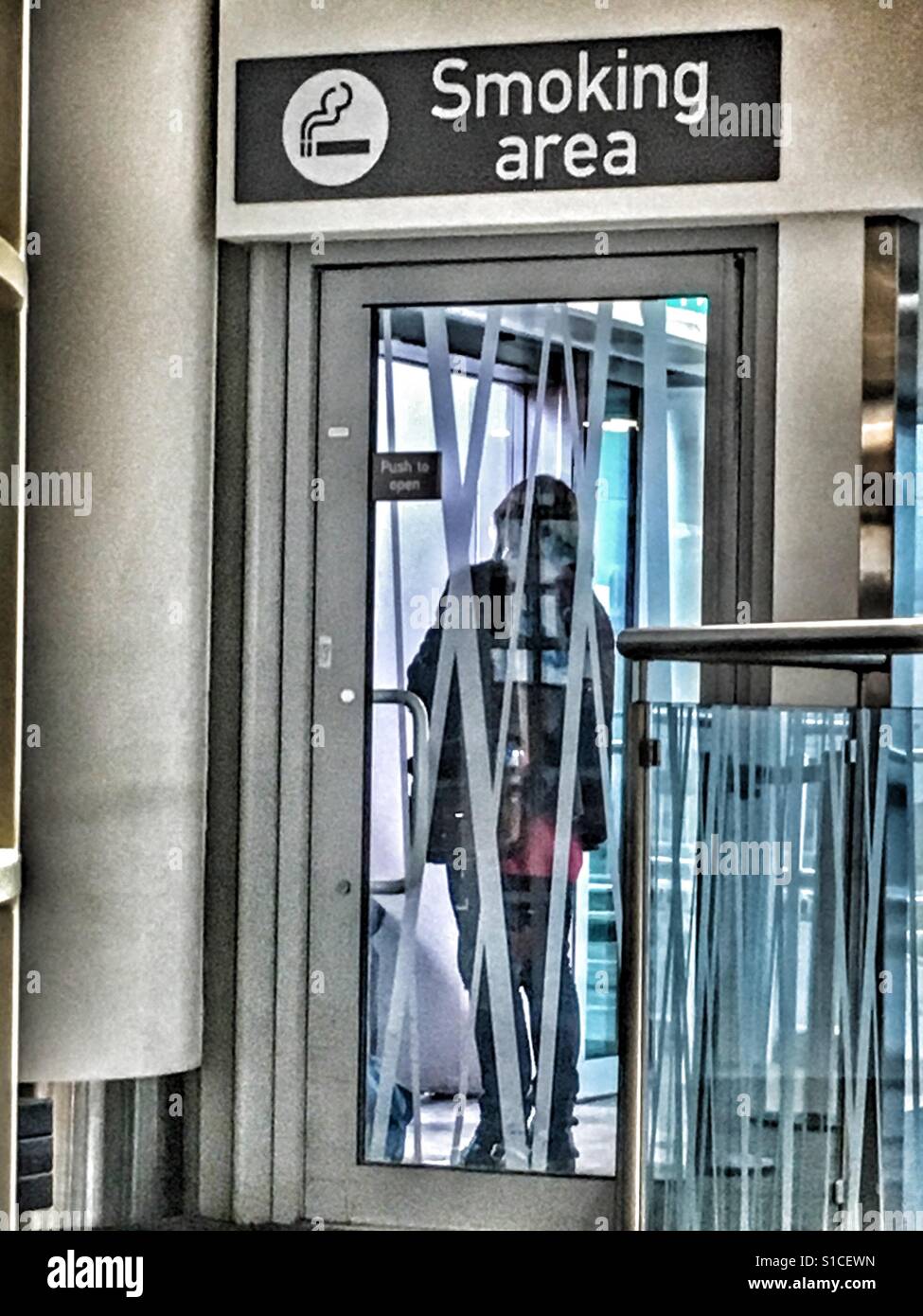 Person behind the closed glass door of the Smoking Area, Bristol Airport, Uk - Smartphone Captured Stock Image