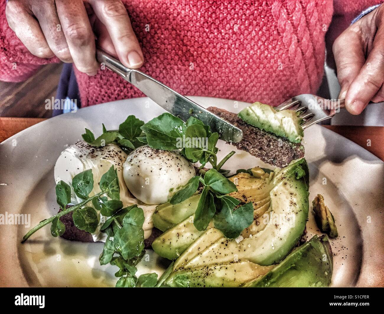 Woman eating a healthy, hearty breakfast: poached eggs on toast and avocado salad - Smartphone Captured Stock Image