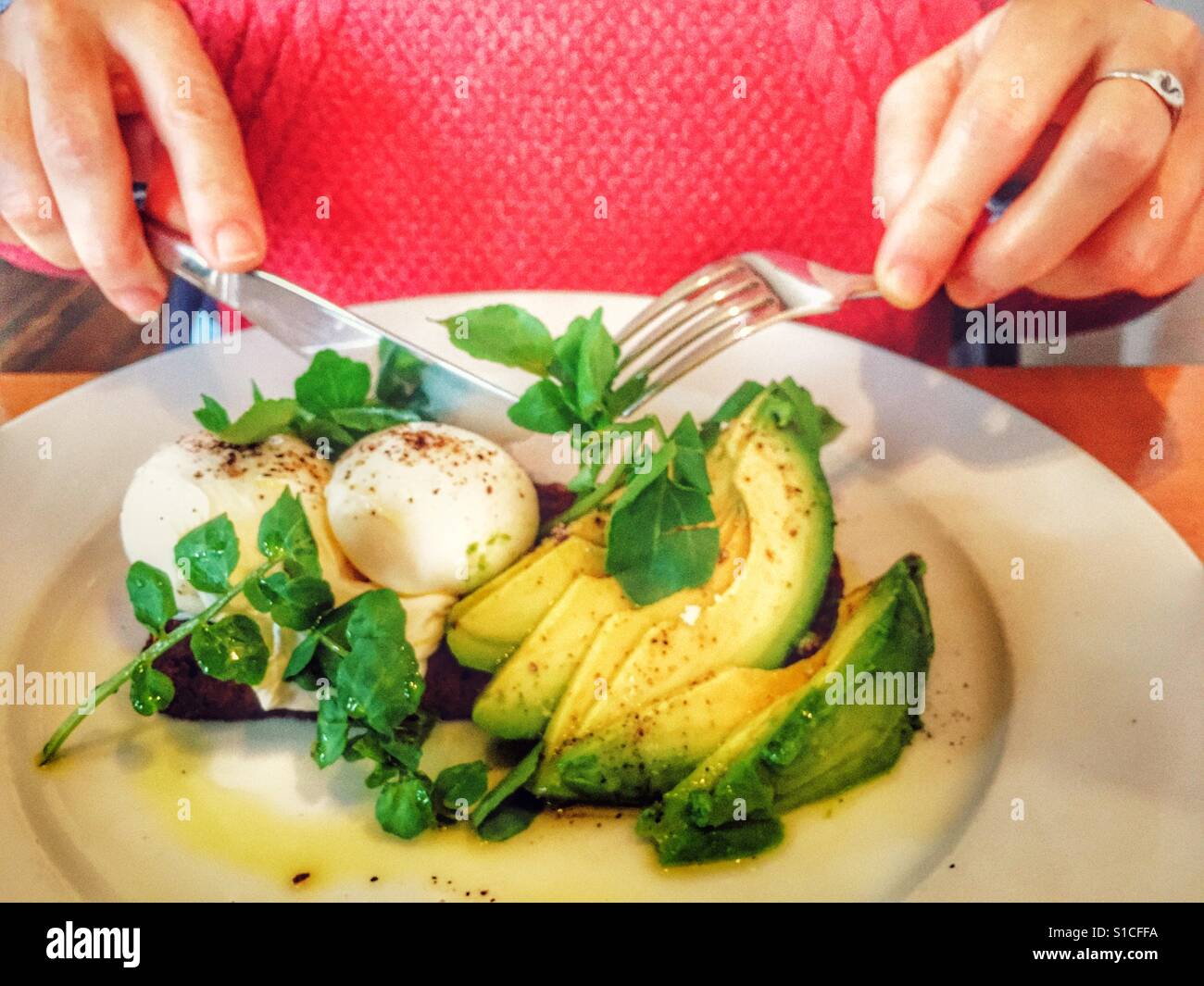 Woman eating poached eggs on toast with avocado salad - Smartphone Captured Stock Image