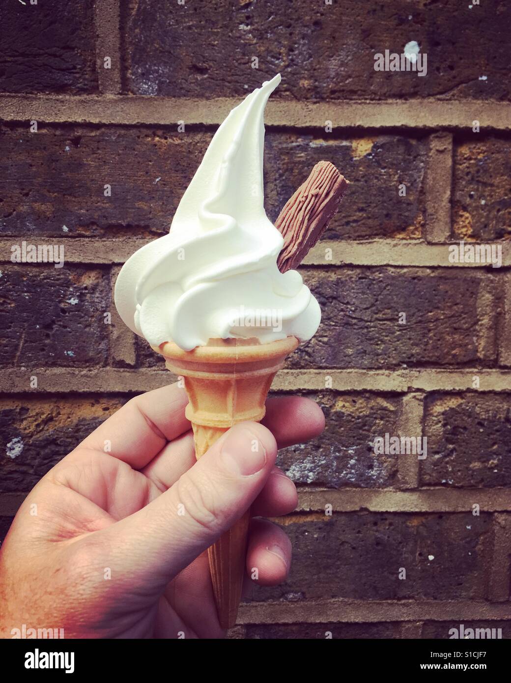Man holding a 99 ice cream against a brick wall - Smartphone Captured Stock Image Man holding a 99 ice cream against a brick wall - Smartphone Captured Stock Image